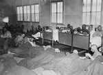 Infirmed survivors lie on cots and on the floor in the infirmary of the Dachau concentration camp.