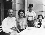 Portrait of an Austrian-Jewish family sitting around a table on a porch.