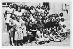 Group portrait of female and child prisoners standing and sitting outside a barrack in the Kraljevica concentration camp.