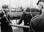 Reichsfuehrer Heinrich Himmler observes two German soldiers, one in a camoulflaged helmut, loading a mortar in an unidentified location.