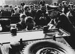 Reichsfuehrer Heinrich Himmler talks with German troops seated in an open military vehicle in an unidentified location.