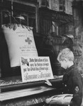 A young boy carrying a loaf of bread under his arm looks at a large sack of flour in the window of a Red Cross food distribution center emblazoned with a sign thanking the American people for their support of the people of France.