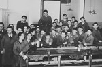 A large group of Jewish youth gather behind a piece of machinery in what probably is a vocational training school in a children's home in Switzerland.