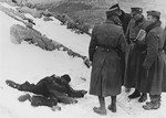 Nazi officials confer together, while a corpse lies nearby in the snow.