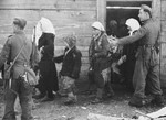 A German soldier escorts Croatian civilians out of a wooden building.