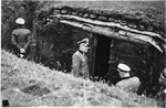 Commandant Hermann Pister, accompanied by two other SS officers, examines a bunker in the Hinzert concentration camp (a sub-camp of Buchenwald).