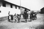 Children stand in a circle with two teachers outside a building in the Rivesaltes internment camp and play a game.