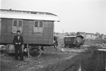 A young Romani man stands in front of a caravan.