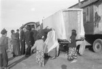 A group of Roma gather alongside a caravan, possibly during a wedding.