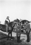 A Romani man holds a horse, as another man sits astride it and a young boy stands in front.