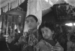 Portrait of a Romani youth holding a child, probably seated inside a caravan.