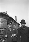 Two Romani men stand in front of a caravan.