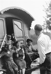 Jan Yoors (with back to the camera) converses with a group of Romani youth seated at the doorway of their caravan.