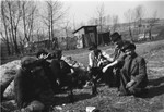 A group of Romani men sit on the ground in a semi-circle, sharing a drink.