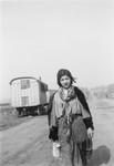 A young Romani woman carrying a container walks down a road.