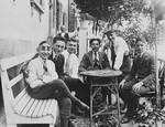 A group of adolescent Jewish friends gather around a small outdoor table in a backyard garden in Breisach.