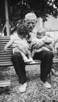 Portrait of a grandfather holding two baby grandchildren on a park bench.