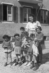 Young children, some holding dolls, pose with their teacher outside a building in a religious kibbutz in Salzburg Austria.