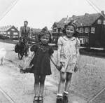 Two young girls, one of whom is a Jewish child in hiding, pose on a street of an unidentified Dutch town in front of a man on a bicycle.