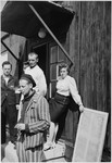 Survivors of Buchenwald, one of whom is smoking a cigarette, stand in front of a barrack.