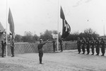 A Nazi soldier salutes as the Nazi and SS flags are raised while a line of troops stand with rifles at attention during the dedication of a new SS hospital in Auschwitz.