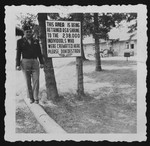 Jospeh H. Williams, deputy-commandant of the Landsberg prison, poses next to a sign marking the site of the crematorium in Dachau that reads, 'This area is being retained a shrine to the 238,000 individuals who were cremated here.