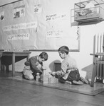 Two young boys sit on the floor underneath a bird cage and build with blocks in a classroom in the Petit Monde children's home.