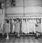 Three little girls dry their hands on towels hanging on hooks in the Petit Monde children's home.