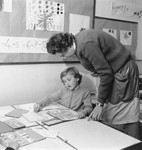 A teacher helps a young girl work on a language exercise in a classroom of unidentified OSE post-war children's home.