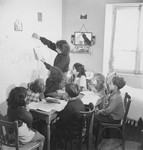 An instructor teaches Hebrew to a group of children seated around a table in an unidentified post-war OSE children's home.