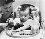 A Dutch-Jewish mother plays with her young baby seated in a high chair.