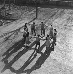 A group of teenagers dances a hora on the grounds of an unidentified post-war OSE children's home.