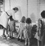A female caregiver helps a group of little girls to wash their hands in the Petit Monde children's home.