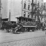 Horse-drawn streetcars and rickshaws ride down a street in the Warsaw ghetto.
