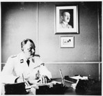 The commander of Gross-Rosen, SS-Obersturmbannfuehrer Arthur Roedl sits at his desk in his office with a photograph of Adolf Hitler hanging on the wall.