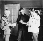 The commander of Gross-Rosen, SS-Obersturmbannfuehrer Arthur Roedl reads from book in the company of two other SS men in his office.