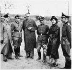A group of SS officers, a woman and a dog stand on the grounds of the Gross-Rosen concentration camp.