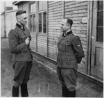 Two SS officers stand and talk outside of a building at the Gross-Rosen concentration camp.