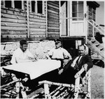 SS officers and an unidentified man sit at a picnic table outside a building at the Gross-Rosen concentration camp.
