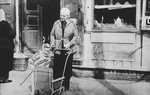A Jewish toddler stands next to his stroller, alongside his Lithuanian nanny.