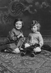 Lore and Erich Rothheimer sit on an oriental rug next to a toy airplane.