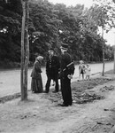 A Romani woman talks with two policemen alongside a road.