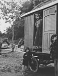 A young Roma woman looks out from the doorway of a caravan, as a young child stands next to it.