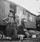 Romani women and children stand outside a caravan.
