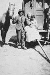 A Romani family outside their caravan.  

A woman and child are seated at the entrance to their caravan; a man stands next to them holding a horse.
