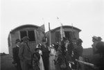 A group of Roma gather in front of two caravans adorned with banners, possibly for a wedding.
