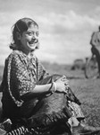 A smiling Romani girl sits with hands clasped in front of her knees.