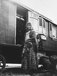 A Romani woman stands outside a caravan.