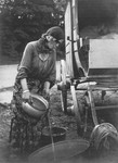 A Romani woman standing next to her caravan pours water from a pot into a laundry tub.