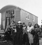 Romani children stand near a caravan, as adults look out from the doorway.